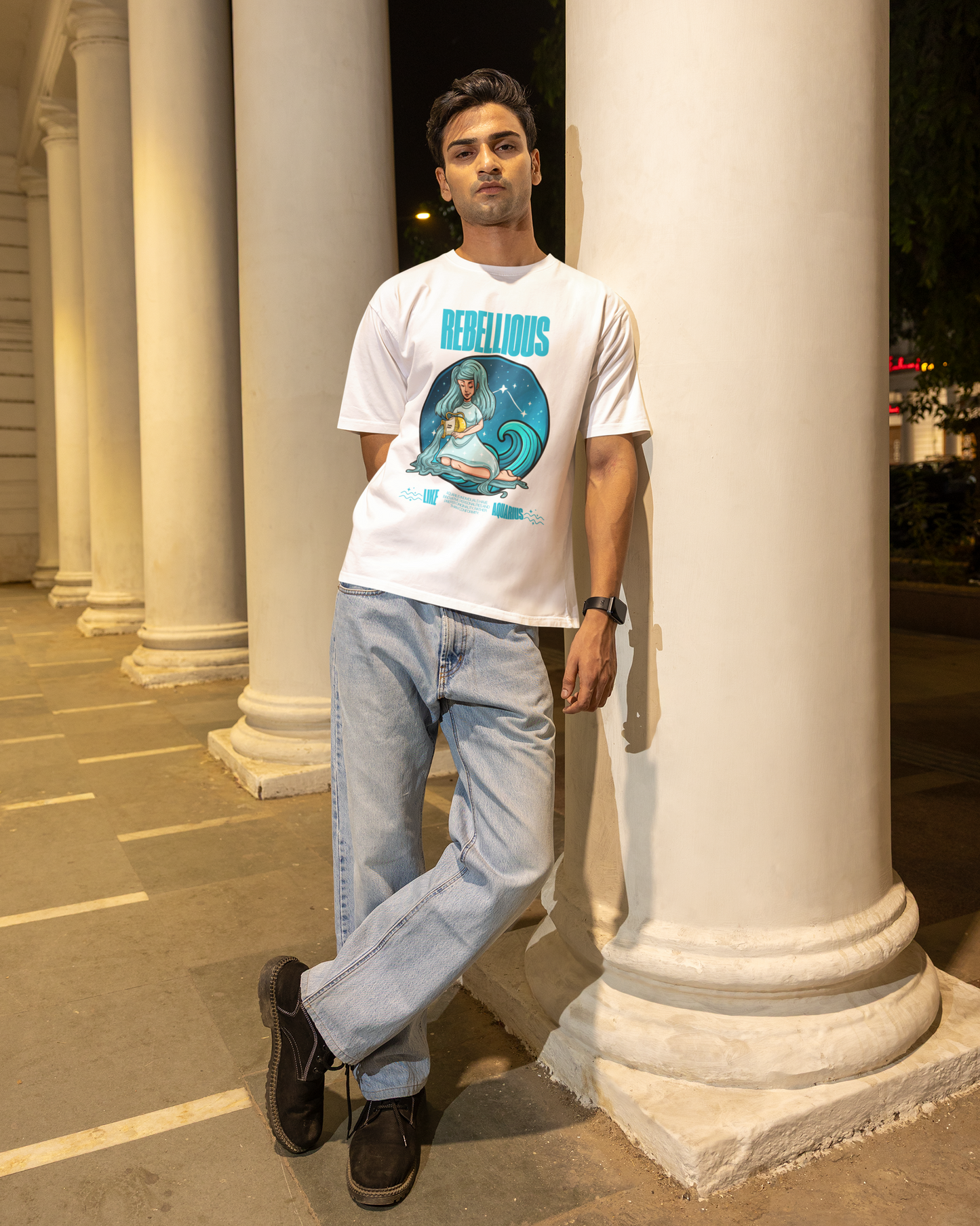 Man wearing a white t-shirt with a graphic design, standing against classical columns at night.