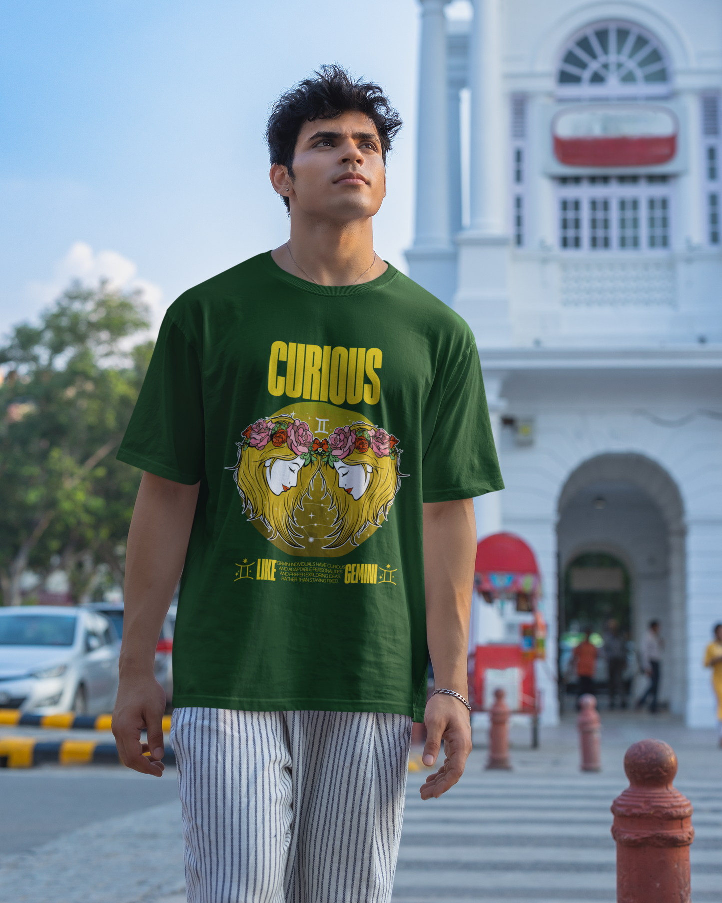Man wearing a green t-shirt with a graphic design and text, standing in front of a white building.