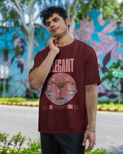 Person wearing a maroon t-shirt with a graphic design in an outdoor setting with trees and a colorful mural.